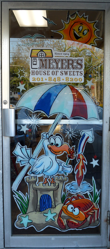 Summer Window Door Painting at Meyer's House of Sweets in Wyckoff, Bergen County, NJ featuring a seagull and crab lighting fireworks on a sand castle